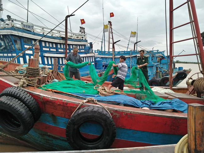 A border guard officer (R) helps fishermen in Quang Tien ward of Sam Son town, the northern central province of Thanh Hoa, prepare for storm Bebinca (Photo: VNA)