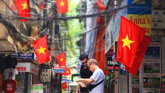 Foreign visitors in a small alley adorned with Vietnamese national flags in Hanoi (Photo: NDO)