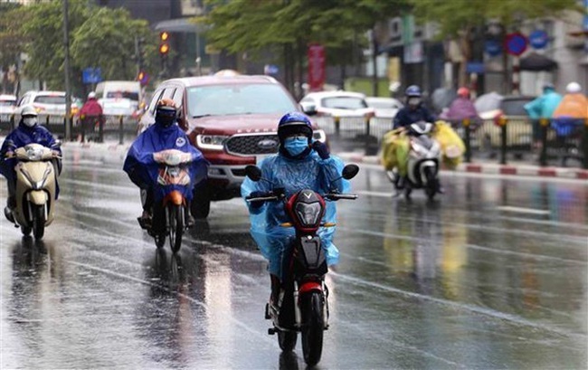 People seen wearing winter clothes drive in the rain (Photo: VNA)